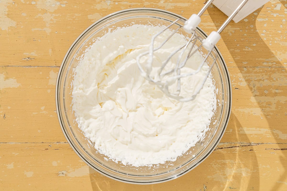 Freshly whipped cream in a bowl next to a hand mixer.