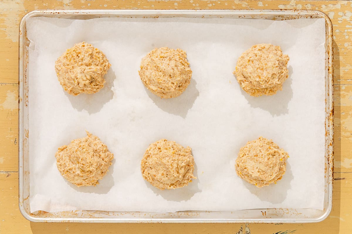 Six unbaked shortcakes on a parchment-lined baking sheet.