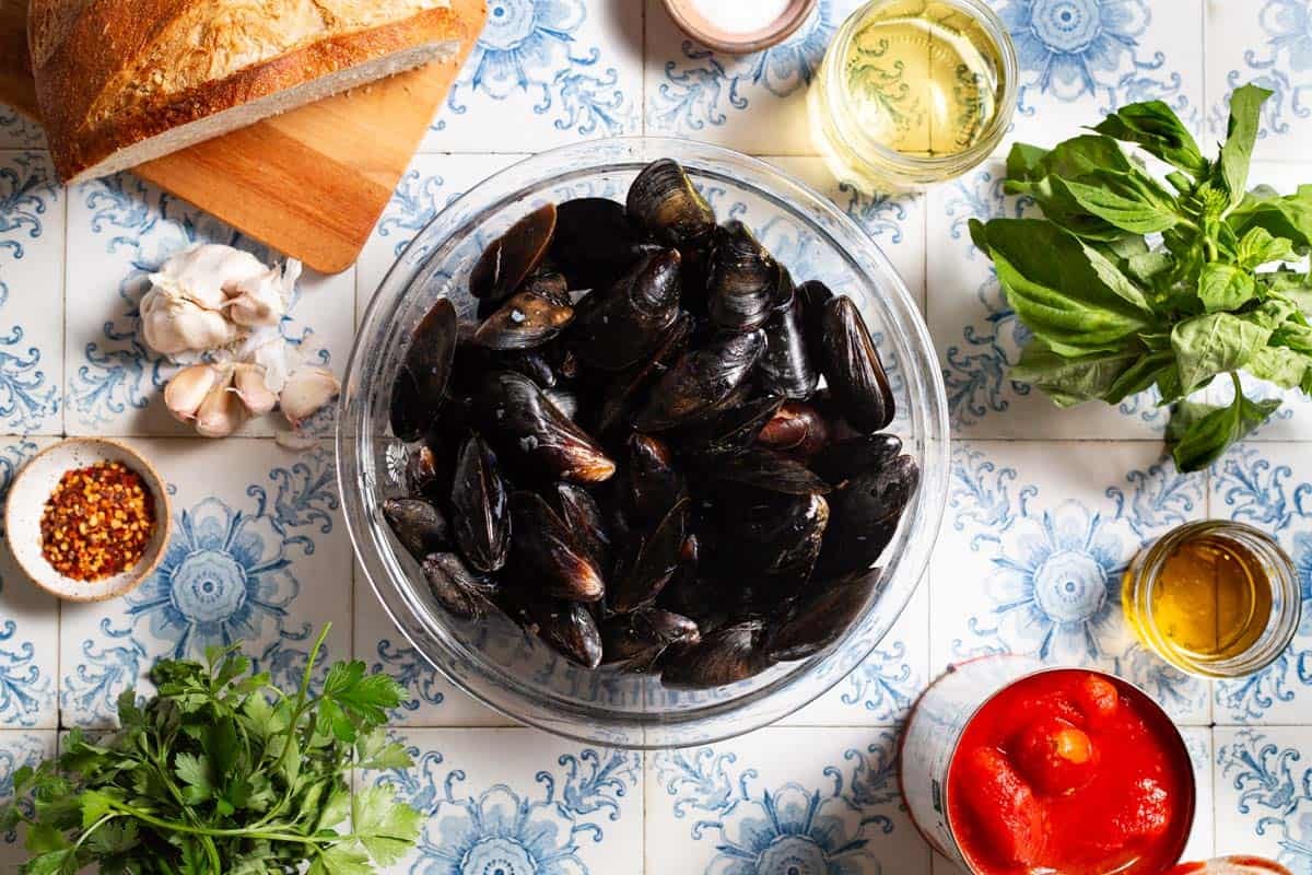 Ingredients for mussels marinara including mussels, olive oil, garlic, red pepper flakes, whole peeled tomatoes, salt, white wine, parsley and basil.