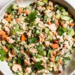 A overhead close up photo of salmon salad in a serving bowl with a spoon next to bowls of capers and parsley.