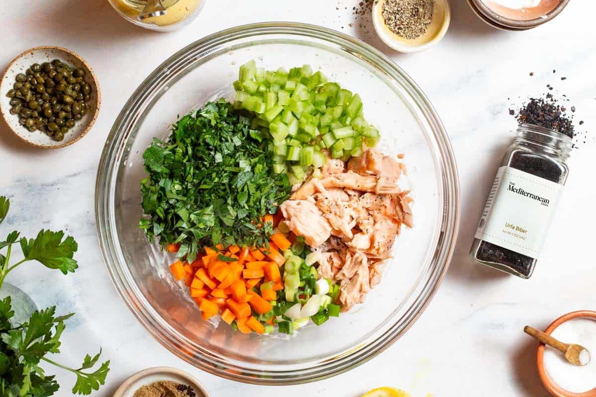 The ingredients for the salmon salad in bowl just before being mixed together. Next to this is urfa biber, parsley, and bowls of capers, pepper and salt.