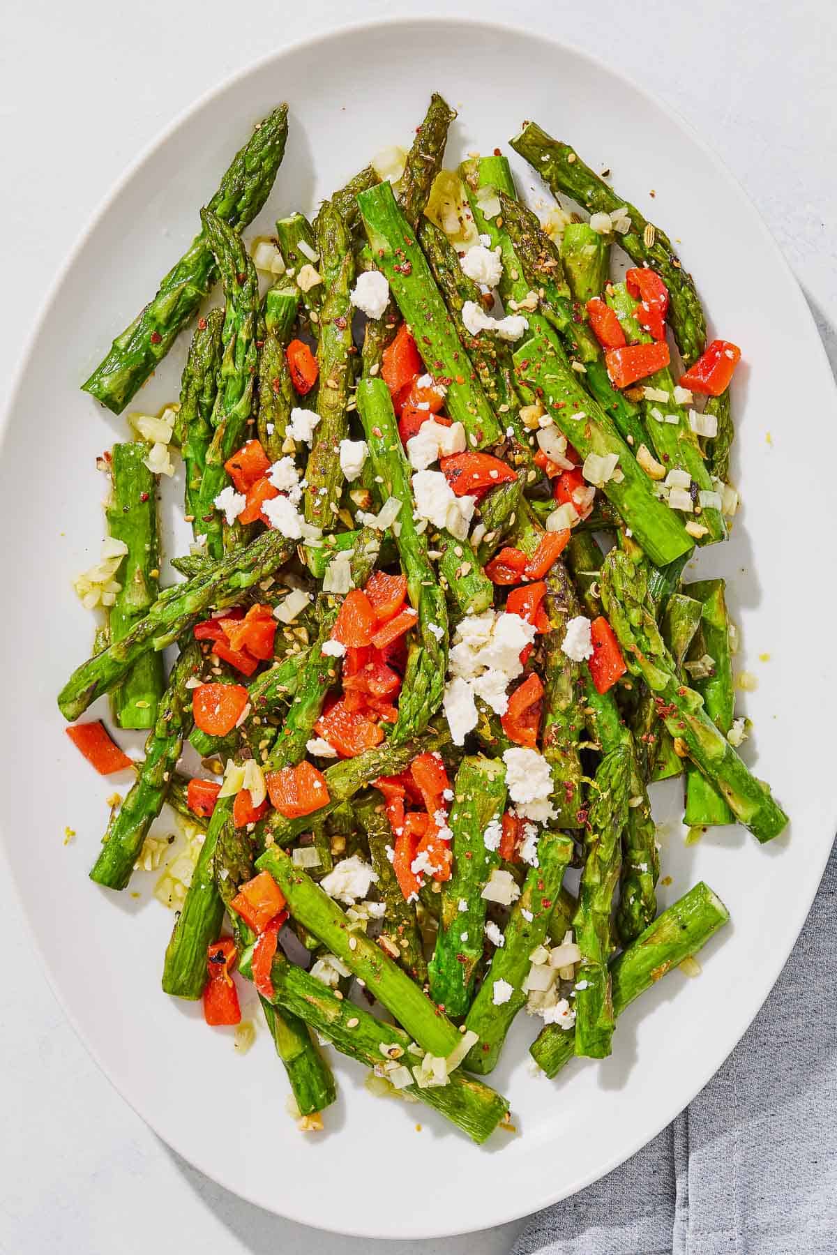 Sauteed asparagus topped with chopped red peppers and crumbled feta on a serving platter.