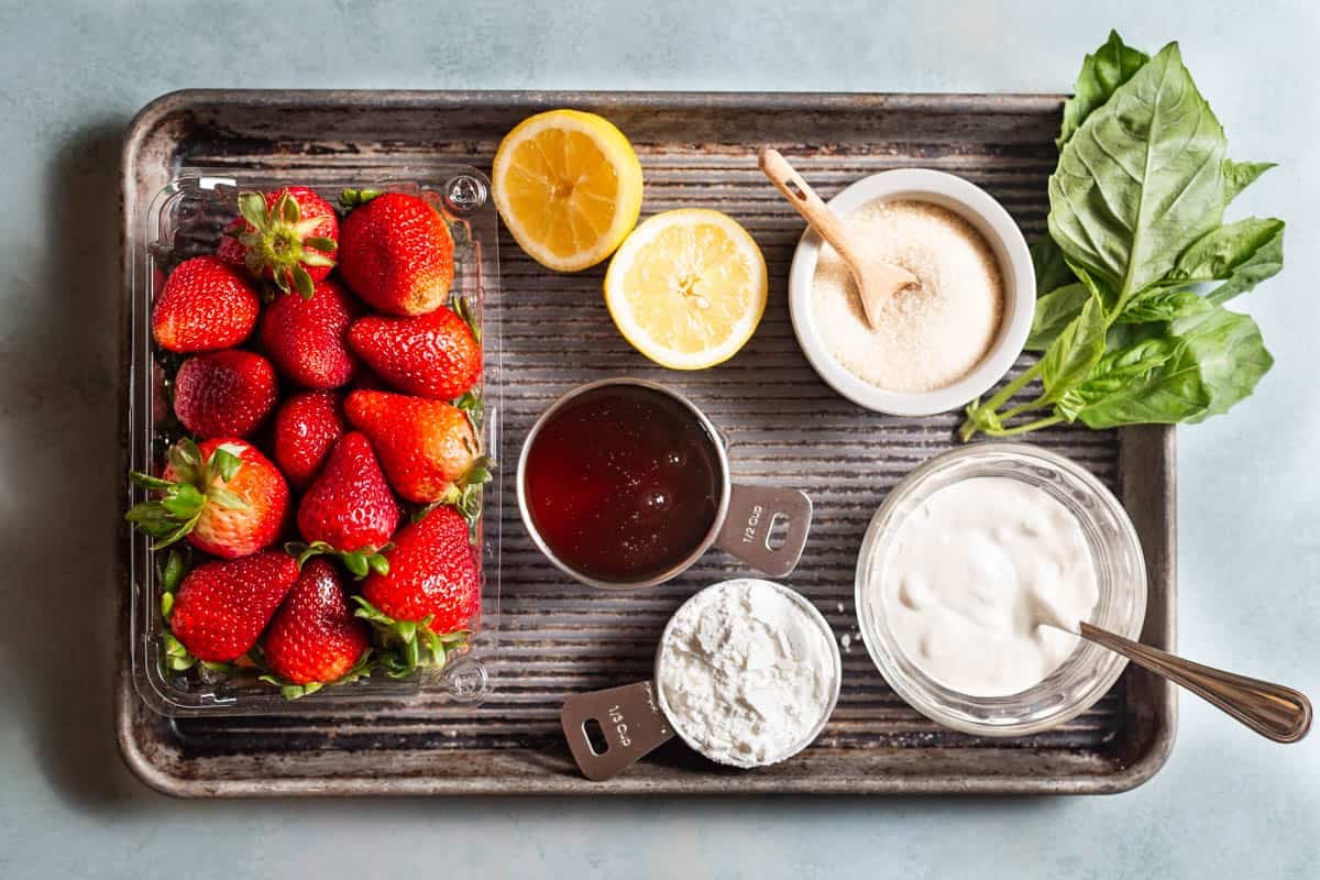 Ingredients for strawberry pudding, including strawberries, cornstarch, sugar, lemon, creme fraiche, honey, and basil.