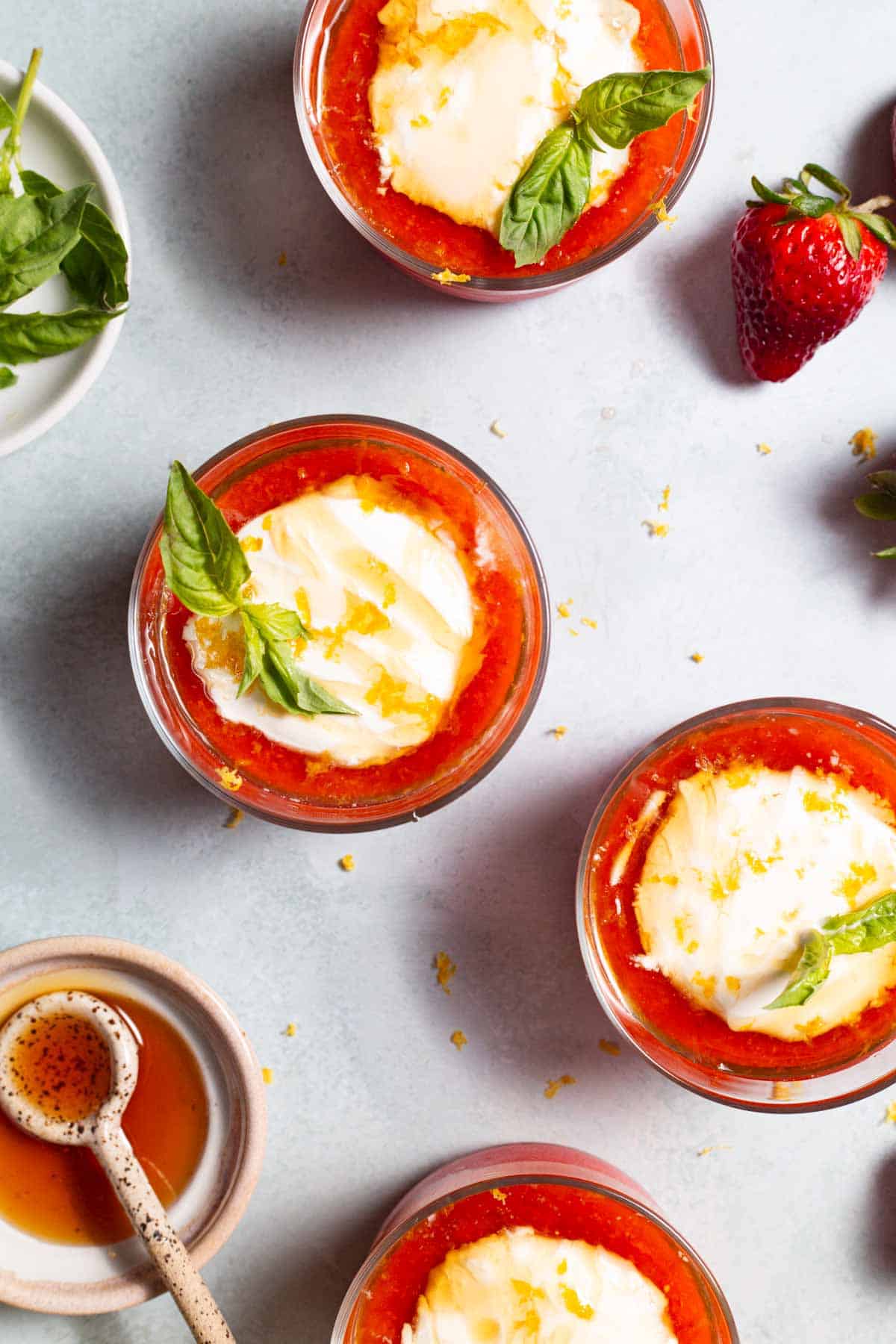 overhead shot of four glasses of strawberry pudding with Crème fraîche, lemon zest, and a sprig of basil on top.