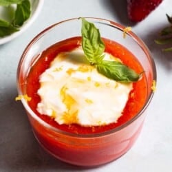 Close up of strawberry pudding with a dollop of Crème fraîche, drizzle of honey, lemon zest and a sprig of basil.