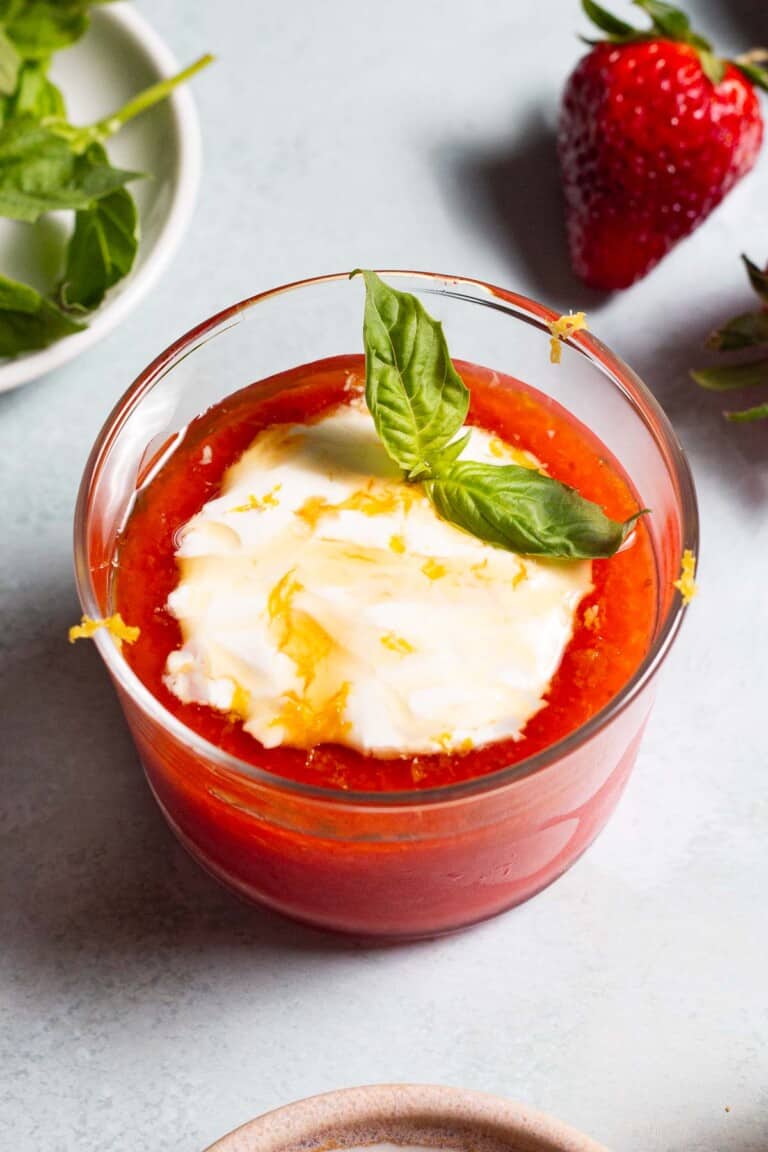 Close up of strawberry pudding with a dollop of Crème fraîche, drizzle of honey, lemon zest and a sprig of basil.