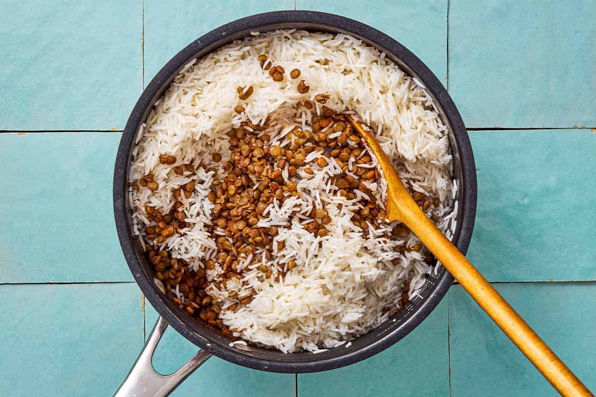 lentils and rice being stirred together in a saucepan.