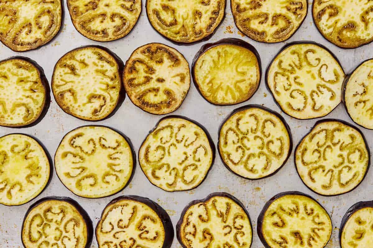 Slices of roasted eggplant arranged in one even layer on a baking sheet.