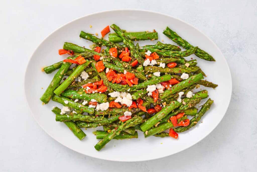 Sauteed asparagus topped with chopped red peppers and crumbled feta on a serving platter.