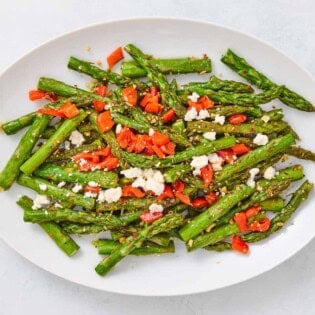 Sauteed asparagus topped with chopped red peppers and crumbled feta on a serving platter.