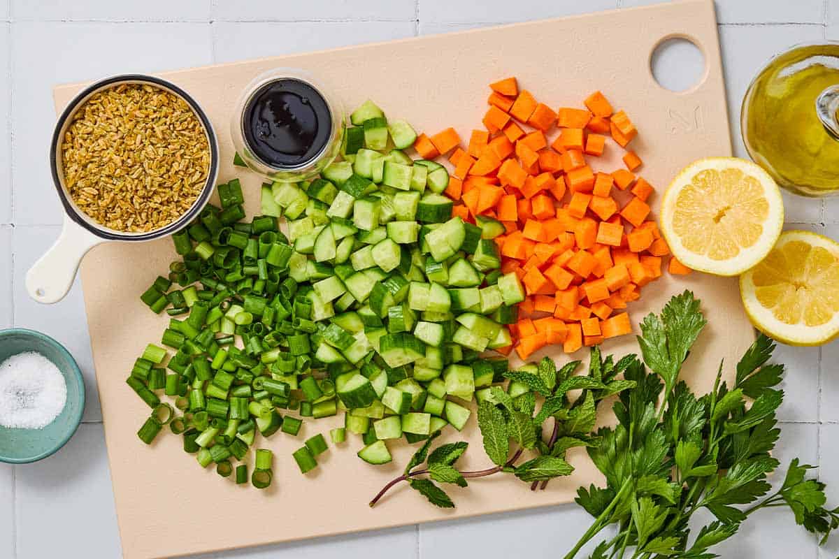 Ingredients for herby freekeh salad including freekeh, salt, green onions, carrots, cucumbers, parsley, mint, lemon, pomegranate molasses and olive oil.