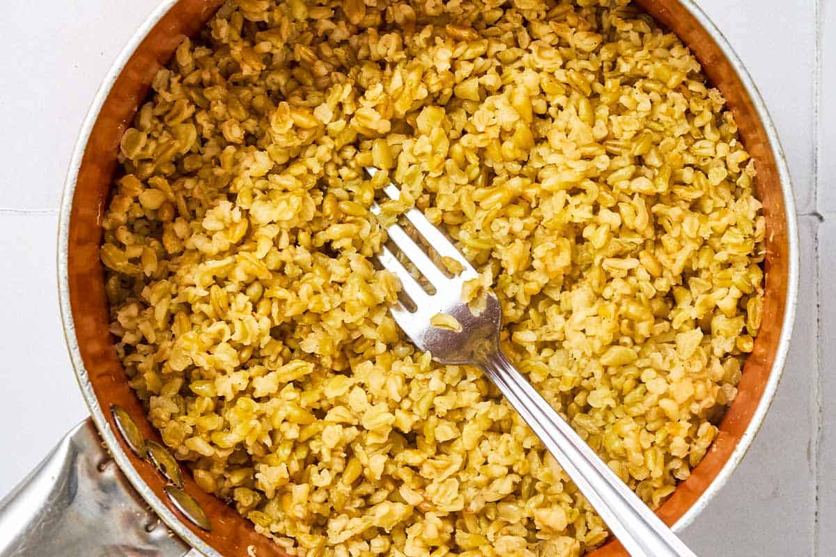 A close up of cooked freekeh in a saucepan with a fork.