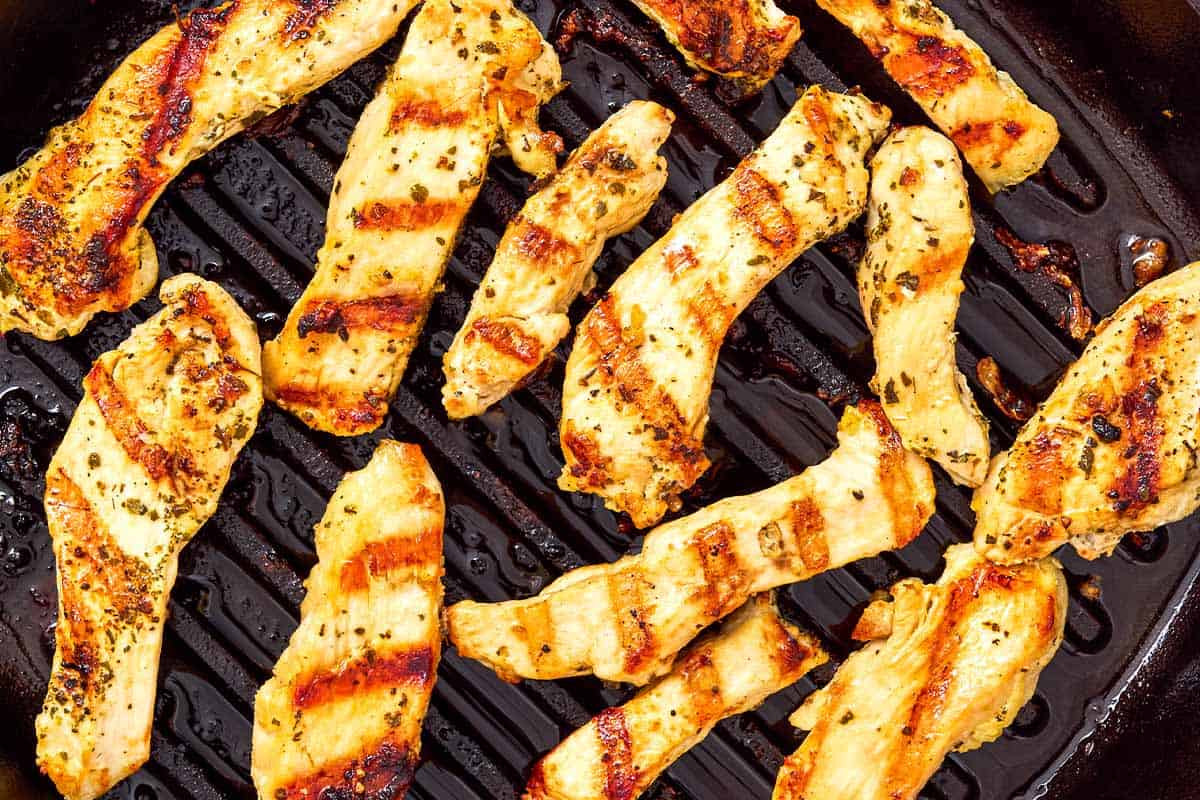Slices of chicken breast being grilled on a cast iron grill pan.