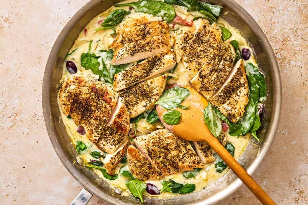 Sun Dried tomato chicken in a skillet with a wooden spoon.