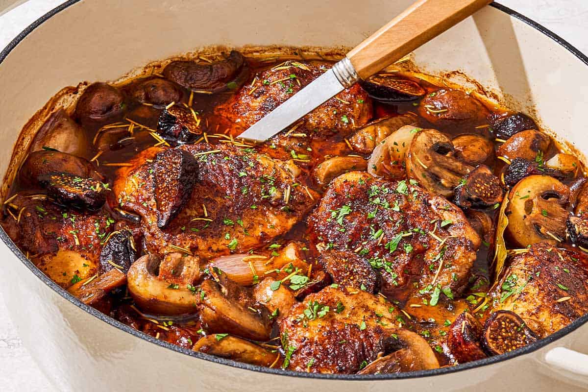 A close up of a pot of wine braised chicken thighs with a serving spoon.