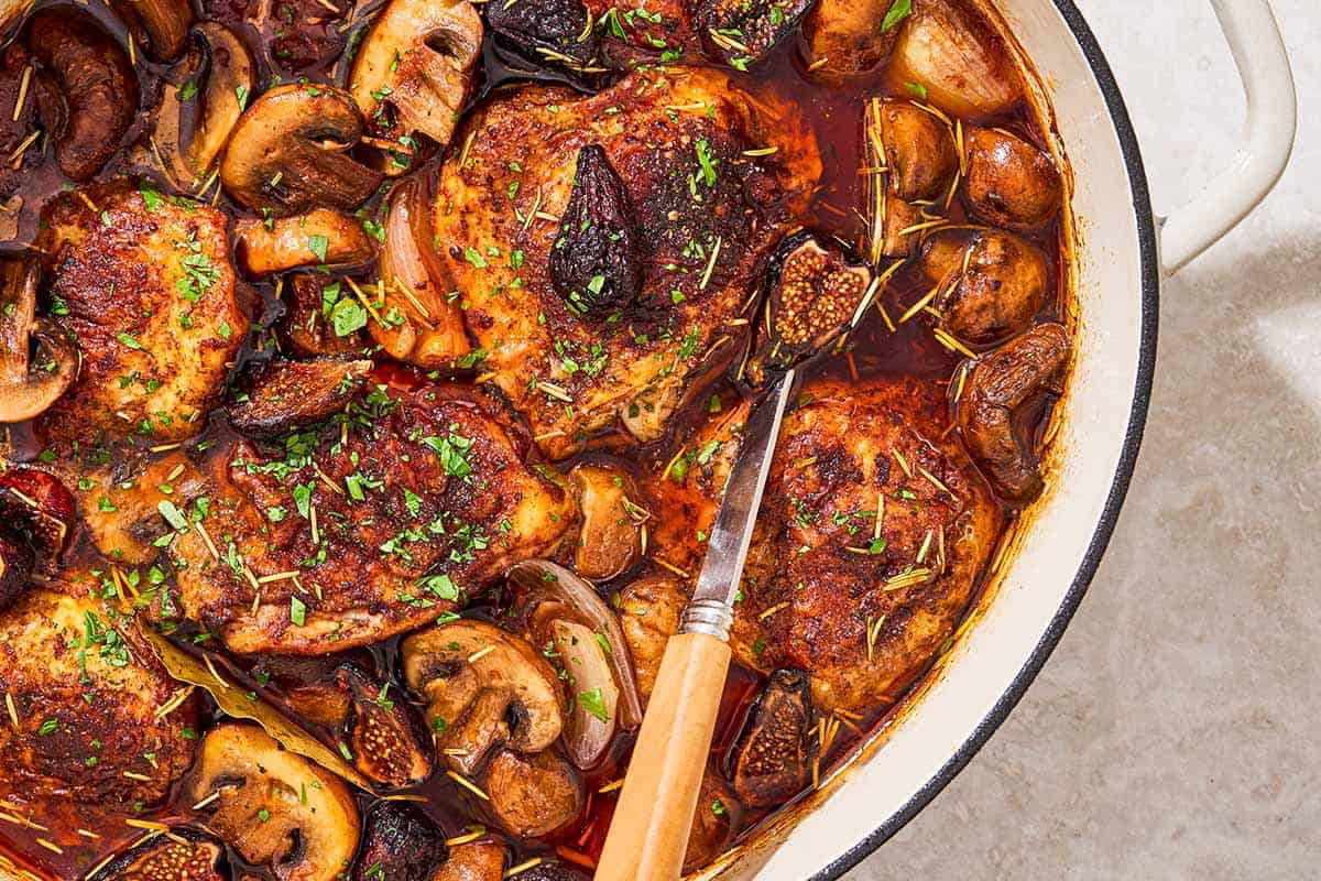 A close up of a pot of wine braised chicken thighs with a serving spoon.