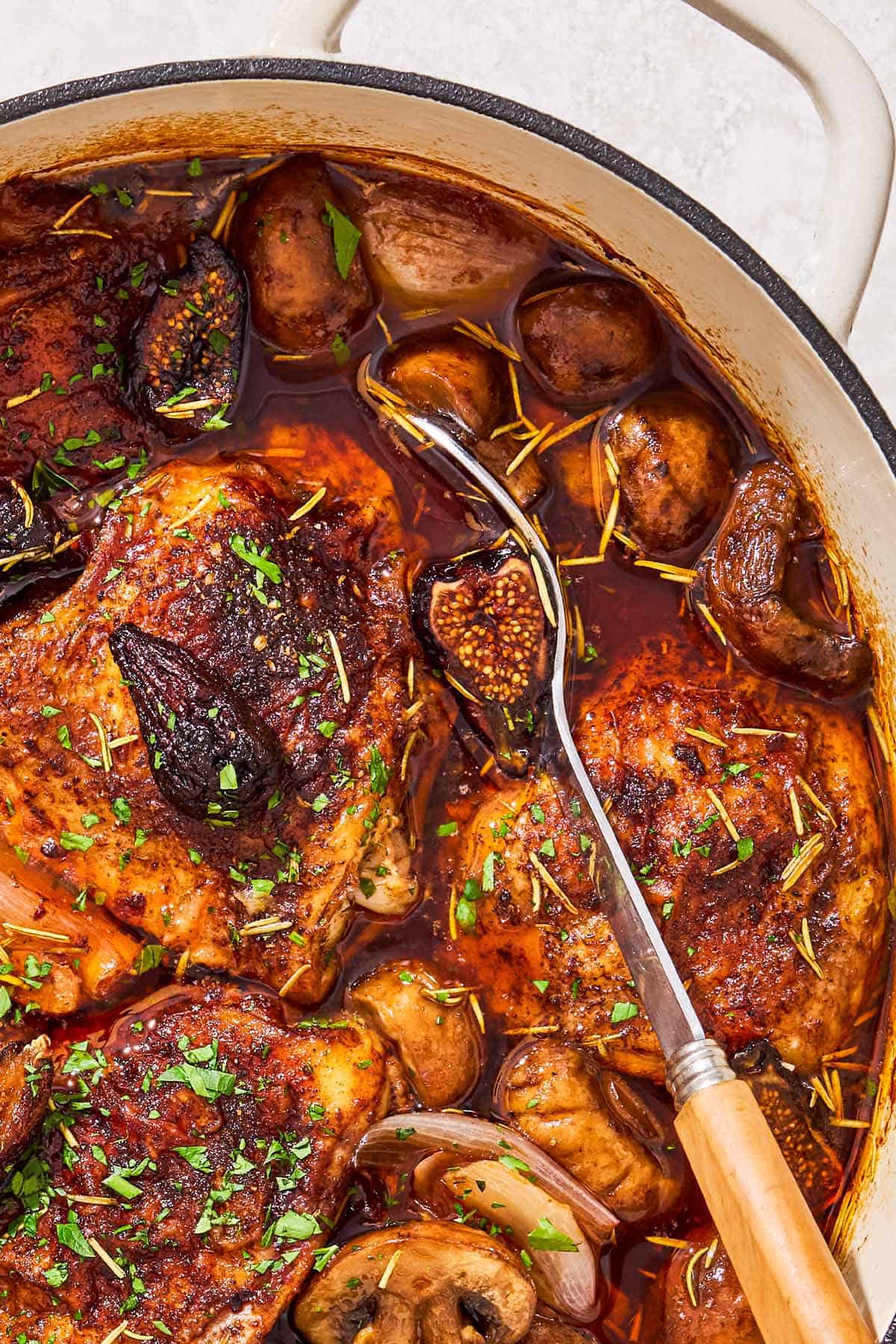A close up of a pot of wine braised chicken thighs with a serving spoon.