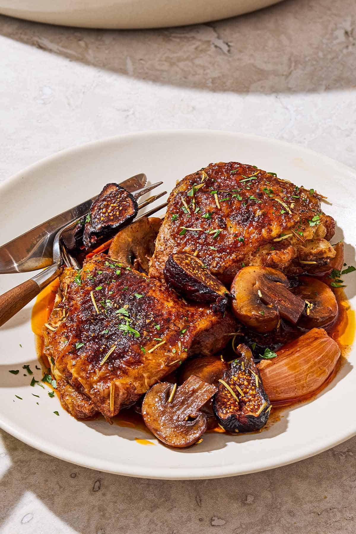 Two wine braised chicken thighs on a plate with a knife and fork.