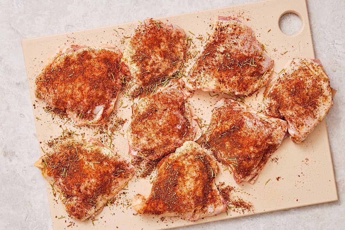 8 seasoned, uncooked chicken thighs on a cutting board.