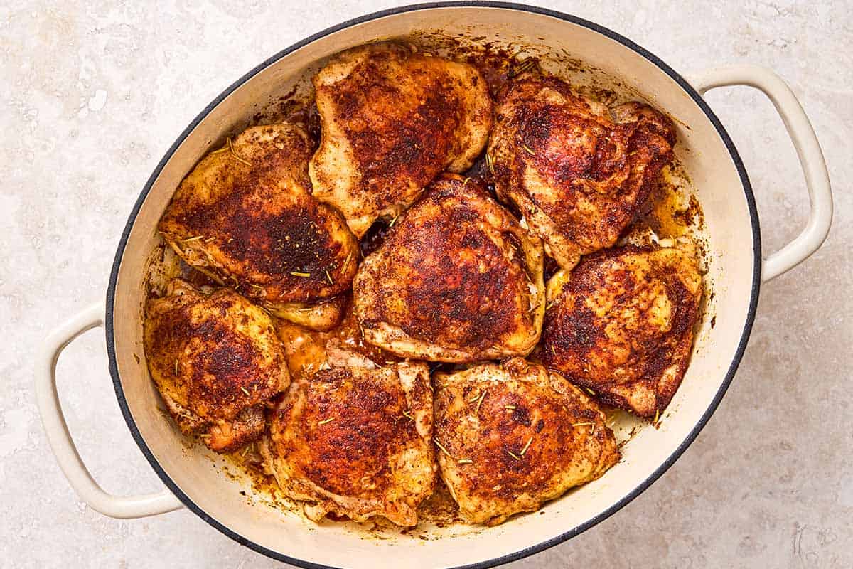 8 seasoned chicken thighs just after being browned in a large pot.