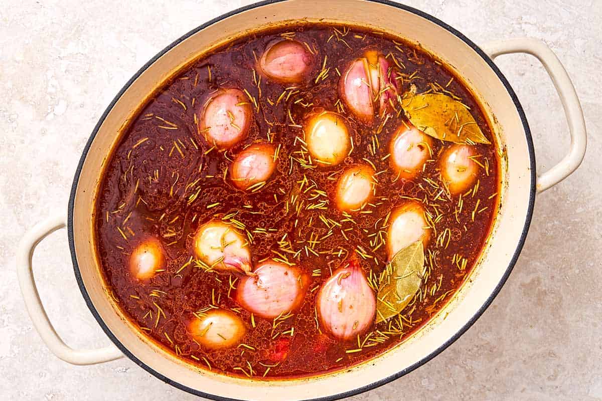 Shallots, garlic, rosemary and bay leaves simmering in tomato paste, wine and chicken broth in a large pot.