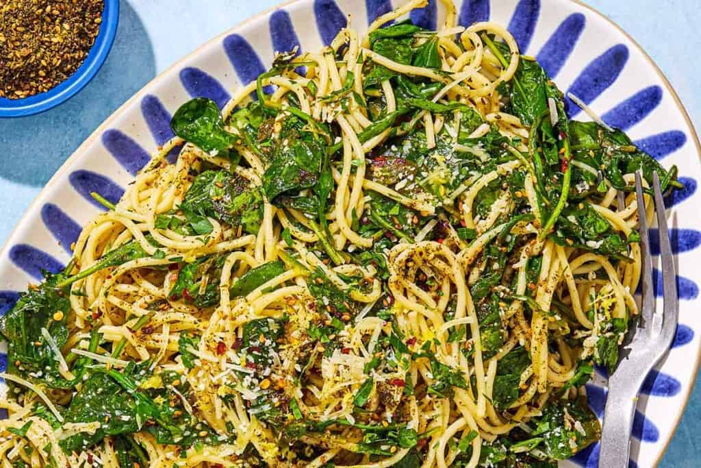 An overhead photo of za'atar garlic spinach pasta on a serving platter with a fork next to a small bowl of za'atar.