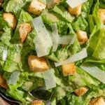 An overhead photo of caesar salad in a serving bowl with serving utensils.