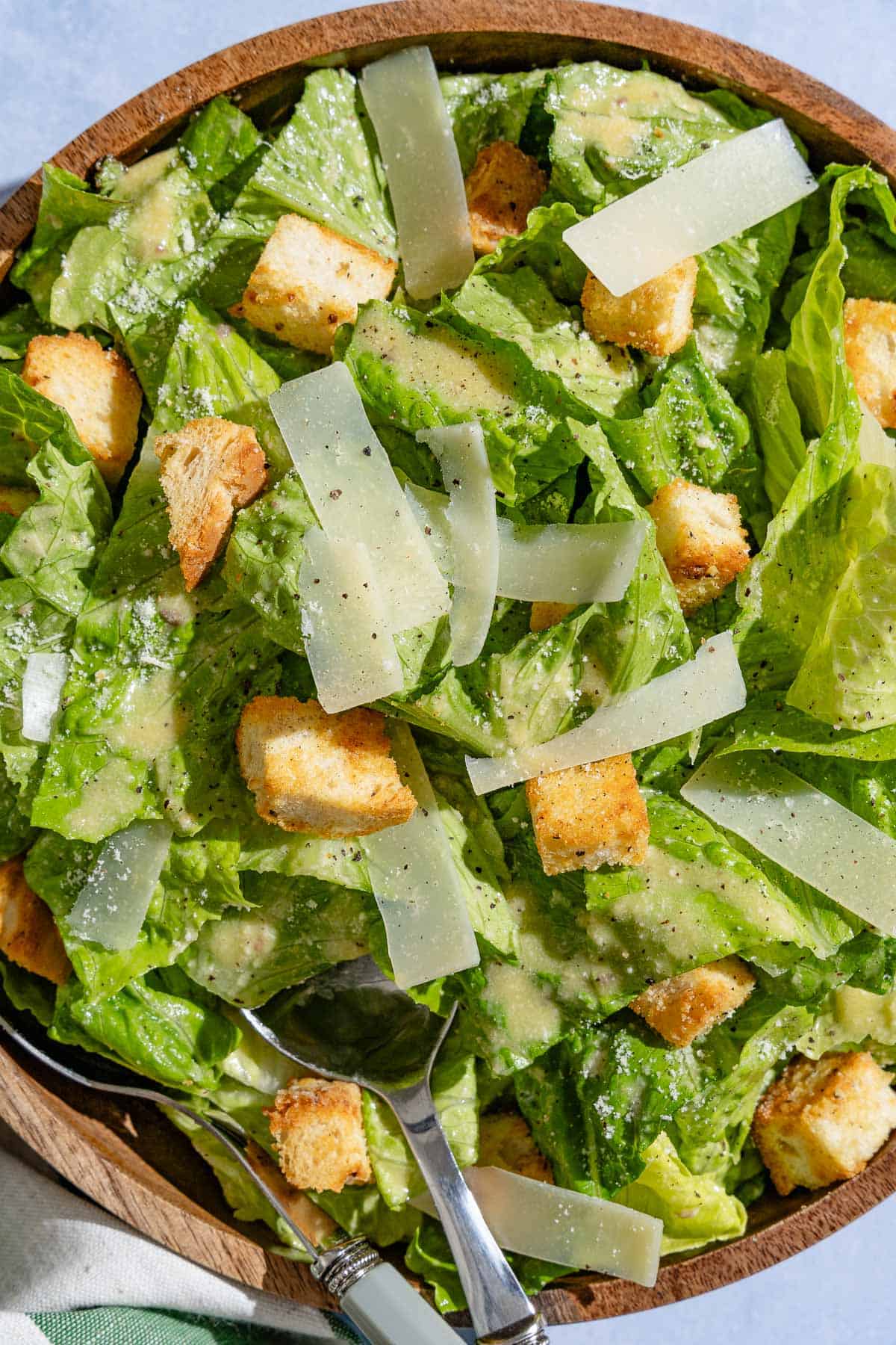 An overhead photo of caesar salad in a serving bowl with serving utensils.