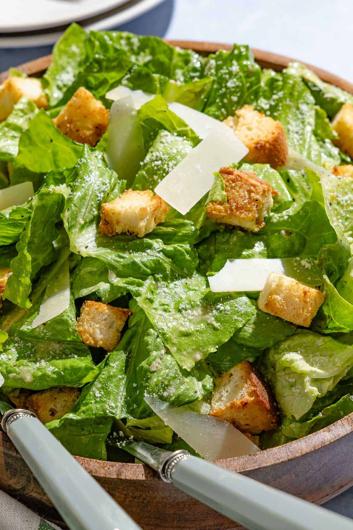 A close up of caesar salad in a serving bowl with serving utensils.