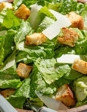 A close up of caesar salad in a serving bowl with serving utensils.