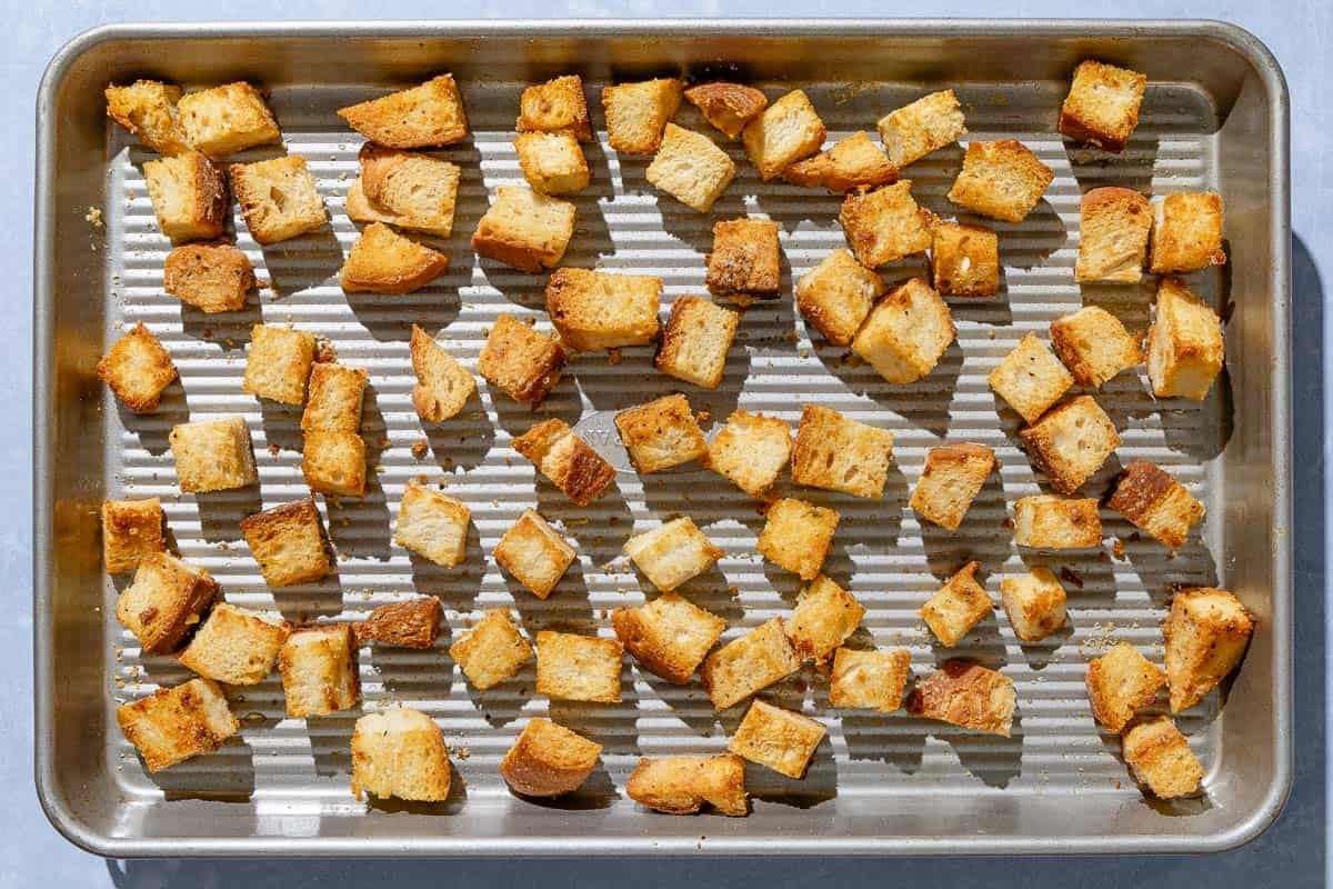 Cubes of baked bread spread evenly on a baking sheet.
