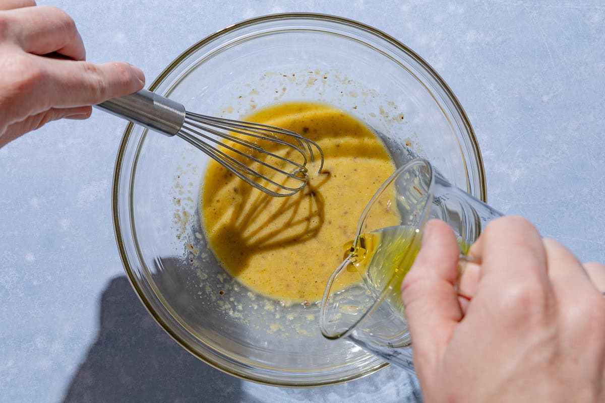 Olive oil being slowly added and whisked with the rest of the caesar salad dressing ingredients.