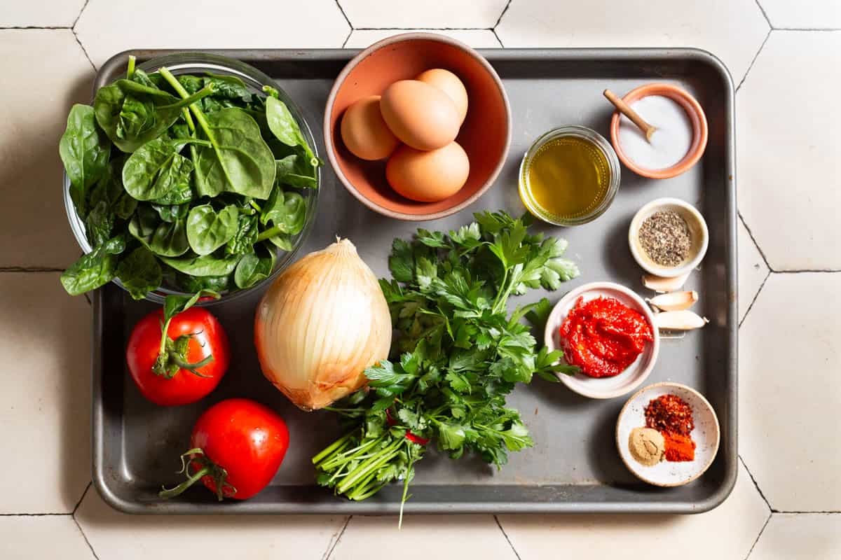 Ingredients for Turkish spinach and eggs, including olive oil, onion, garlic, cumin, paprika, red pepper paste, tomatoes, spinach, salt, pepper, eggs, aleppo pepper, and parsley.