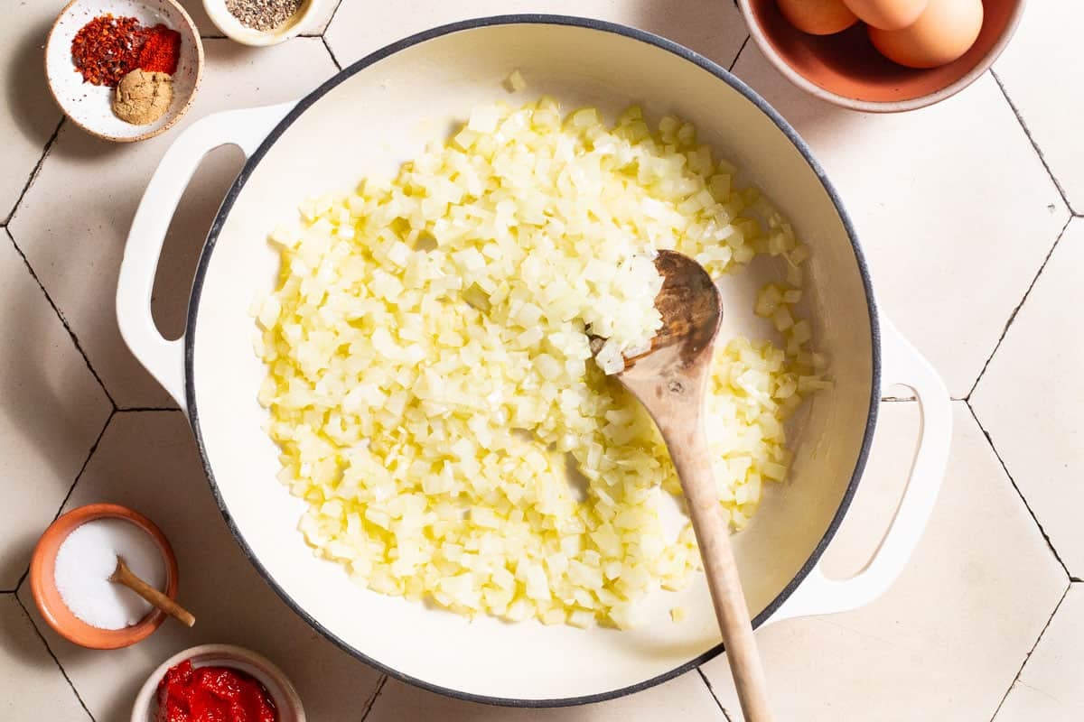 Onions and garlic being mixed in a skillet with a wooden spoon.