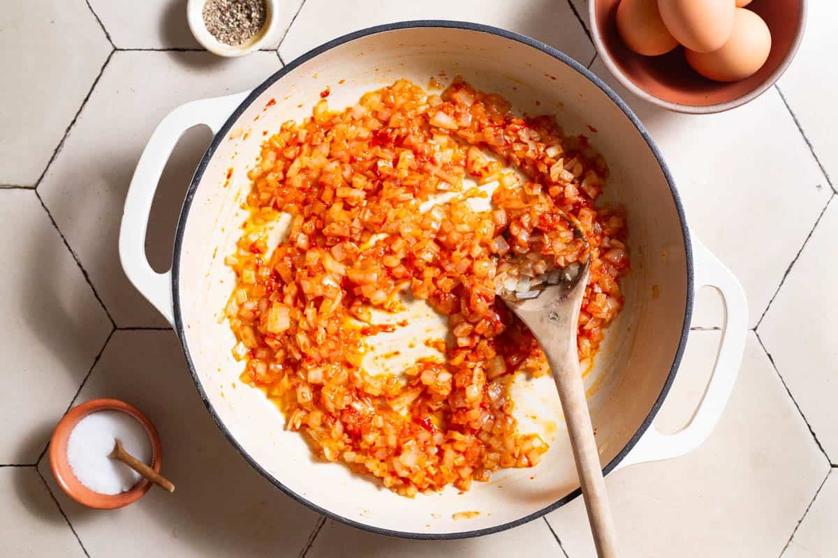 Onions and garlic in a skillet coated in paprika, cumin, and red pepper paste.