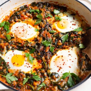 four poached eggs in a saucepan with wilted spinach and fresh parsley.