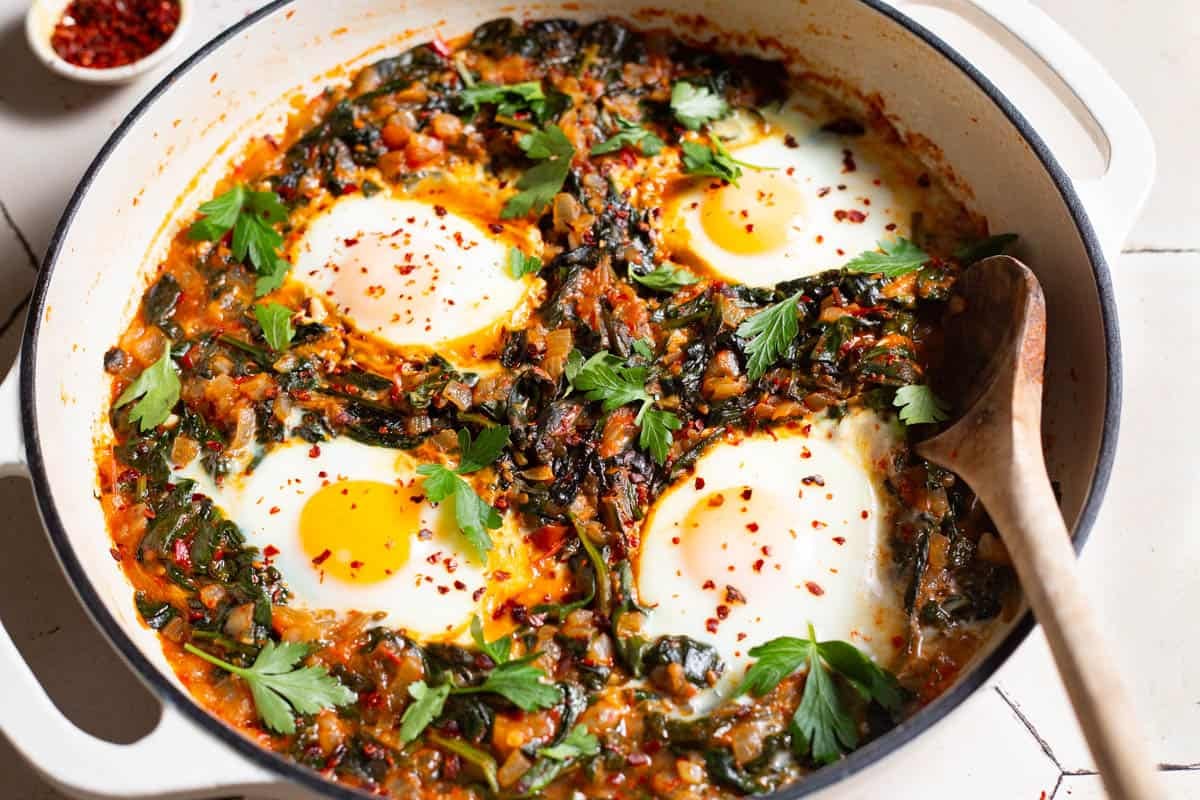 four poached eggs in a saucepan with wilted spinach and fresh parsley.