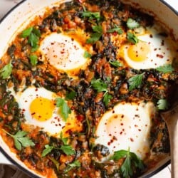 Side shot of a pan with Turkish spinach and eggs, showing the 4 poached eggs and saucy wilted spinach mixture.