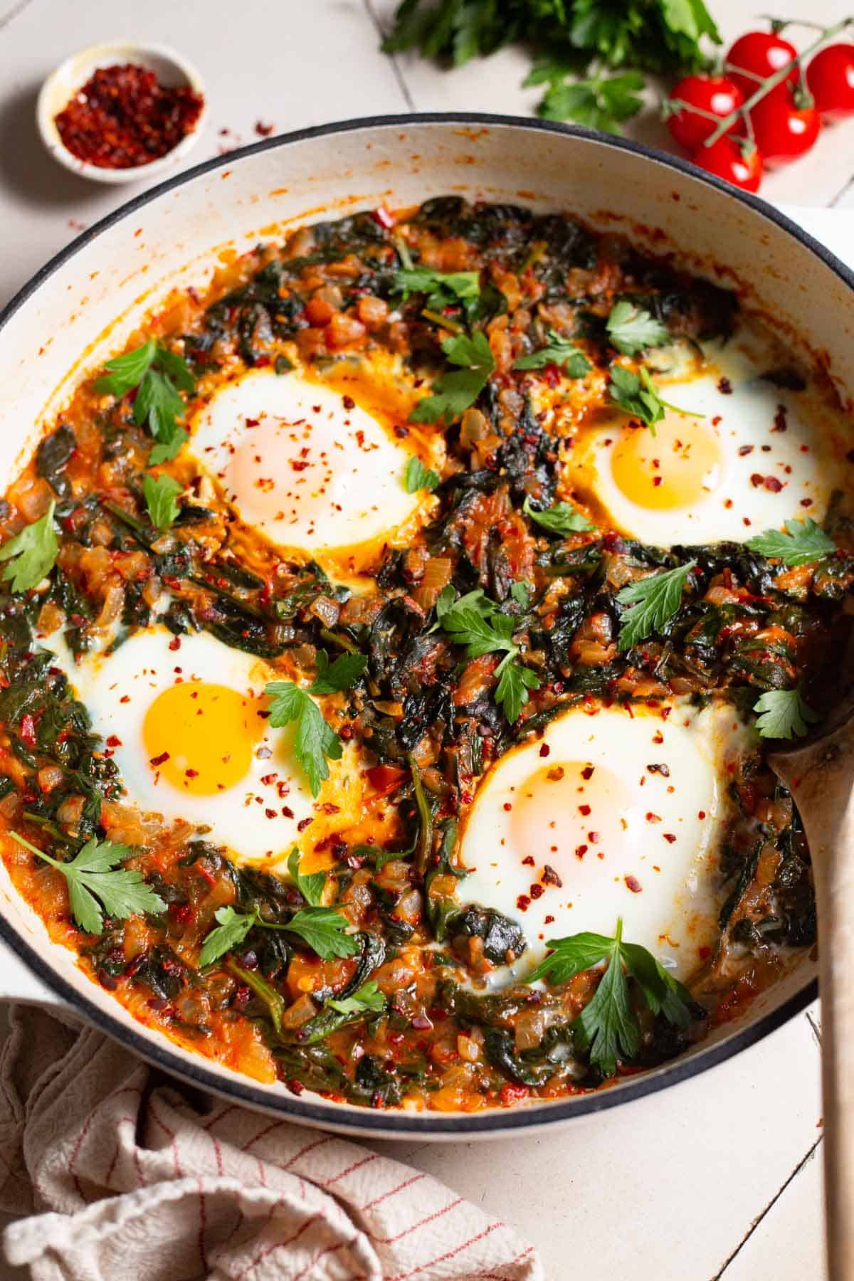 Side shot of a pan with Turkish spinach and eggs, showing the 4 poached eggs and saucy wilted spinach mixture.