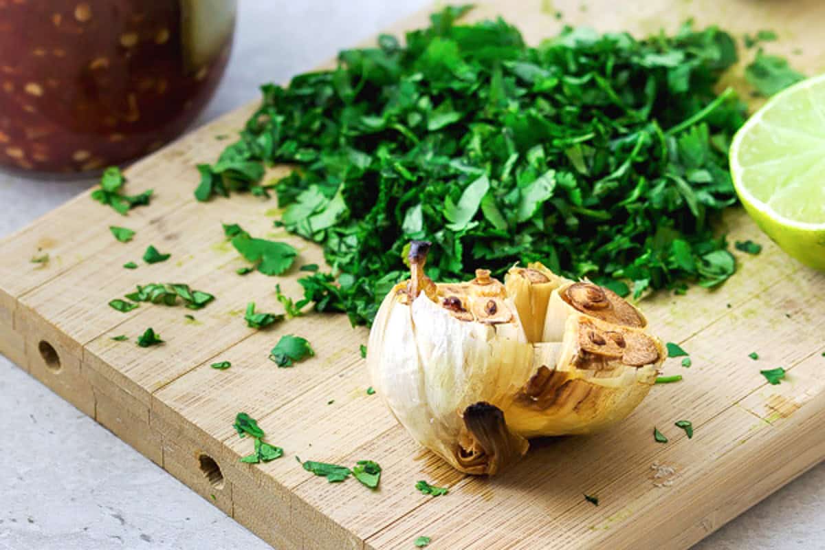 Roasted garlic, chopped parsley and a lime half on a cutting board.