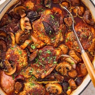 An overhead photo of a pot of wine braised chicken thighs with a serving spoon.