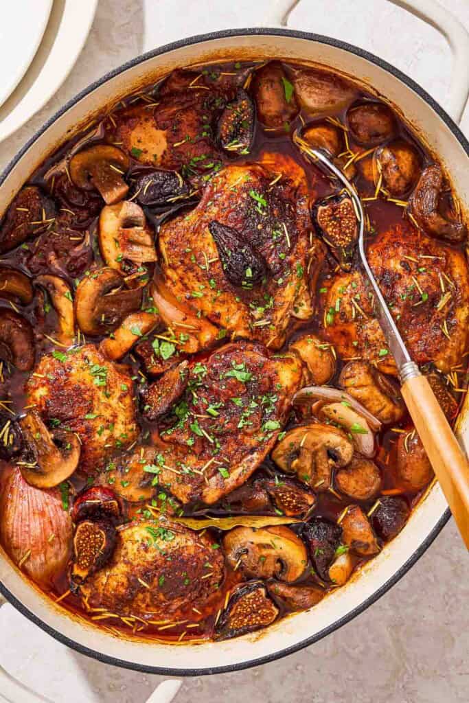 An overhead photo of a pot of wine braised chicken thighs with a serving spoon.