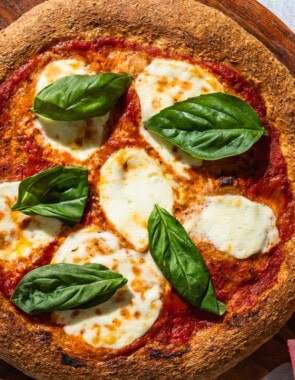 An overhead photo of a pizza with a whole wheat pizza crust on a wooden serving platter with a kitchen towel.