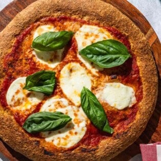 An overhead photo of a pizza with a whole wheat pizza crust on a wooden serving platter with a kitchen towel.
