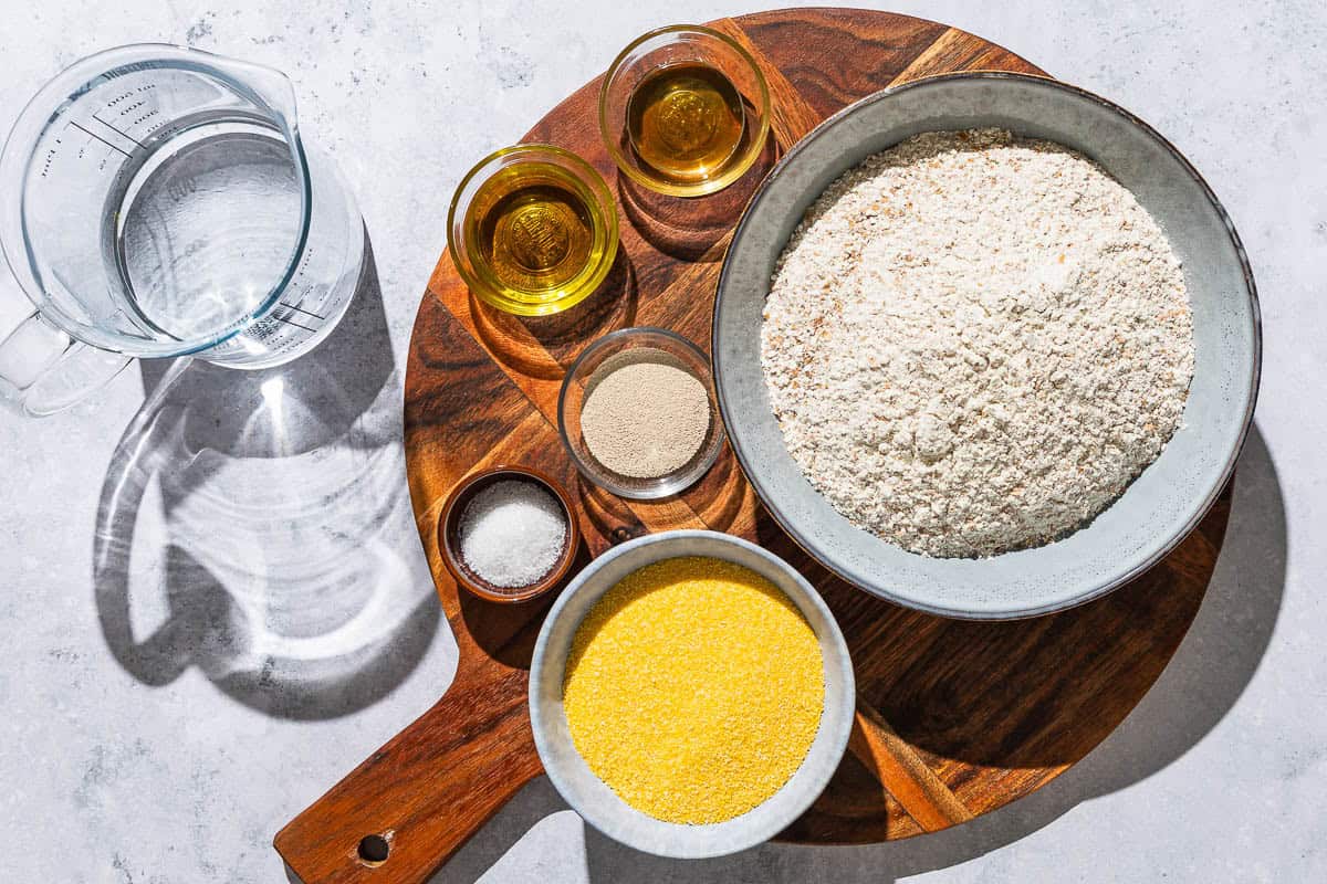 Ingredients for whole wheat pizza dough including whole wheat flour, instant yeast, salt, warm water, olive oil, honey and cornmeal.