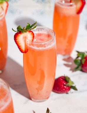Four strawberry bellinis in glasses garnished with strawberry slices surrounded by whole strawberries.