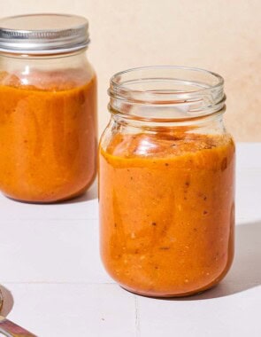 Two jars of roasted tomato sauce, one of them with a lid on it. There is a serving spoon next to the jars.