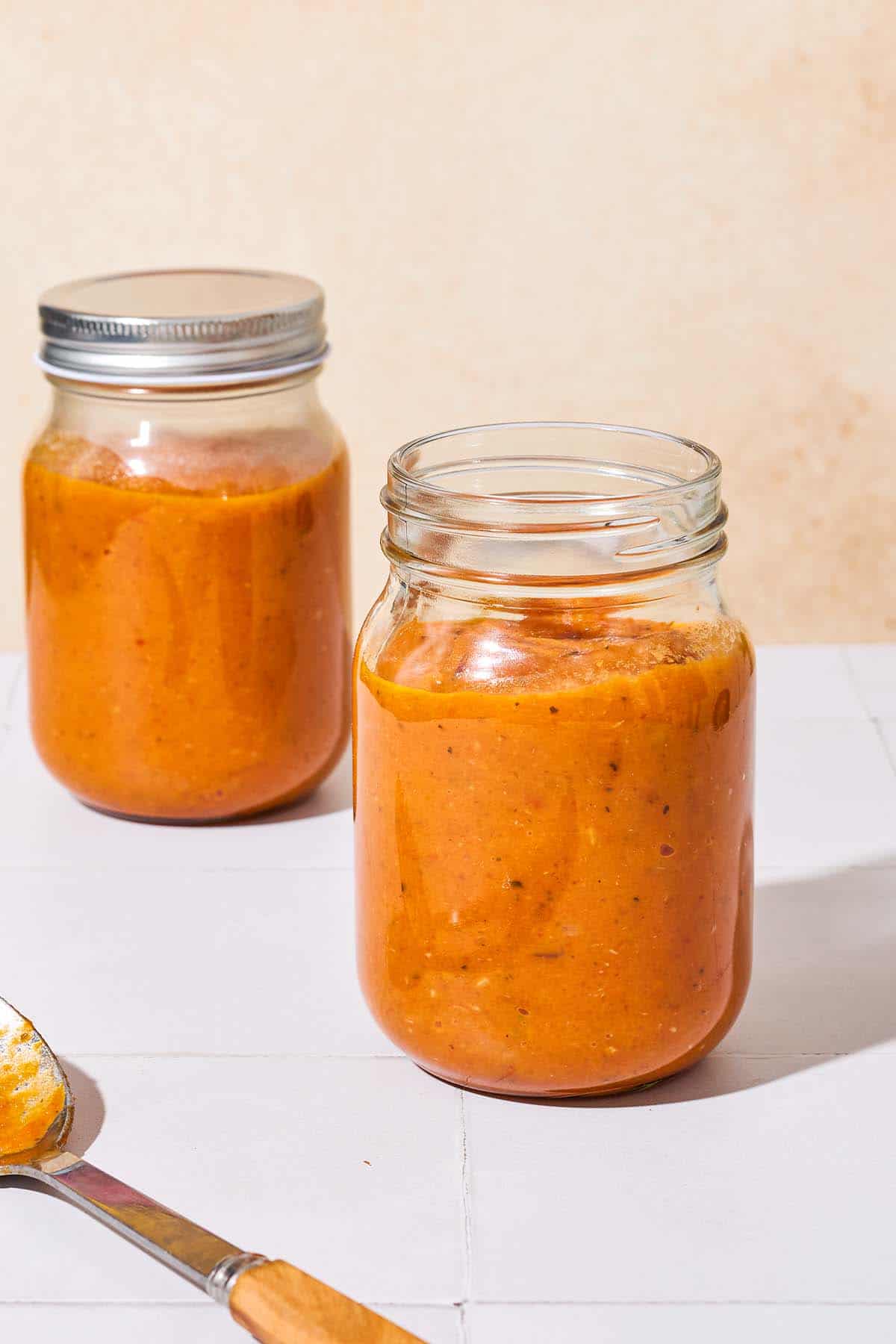 Two jars of roasted tomato sauce, one of them with a lid on it.