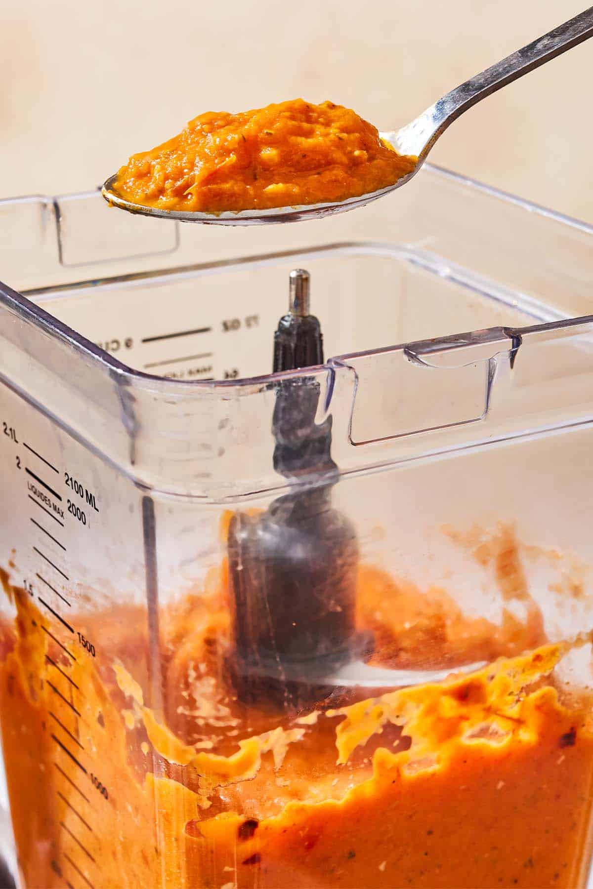 A spoonful of the roasted tomato sauce being lifted out of a blender.