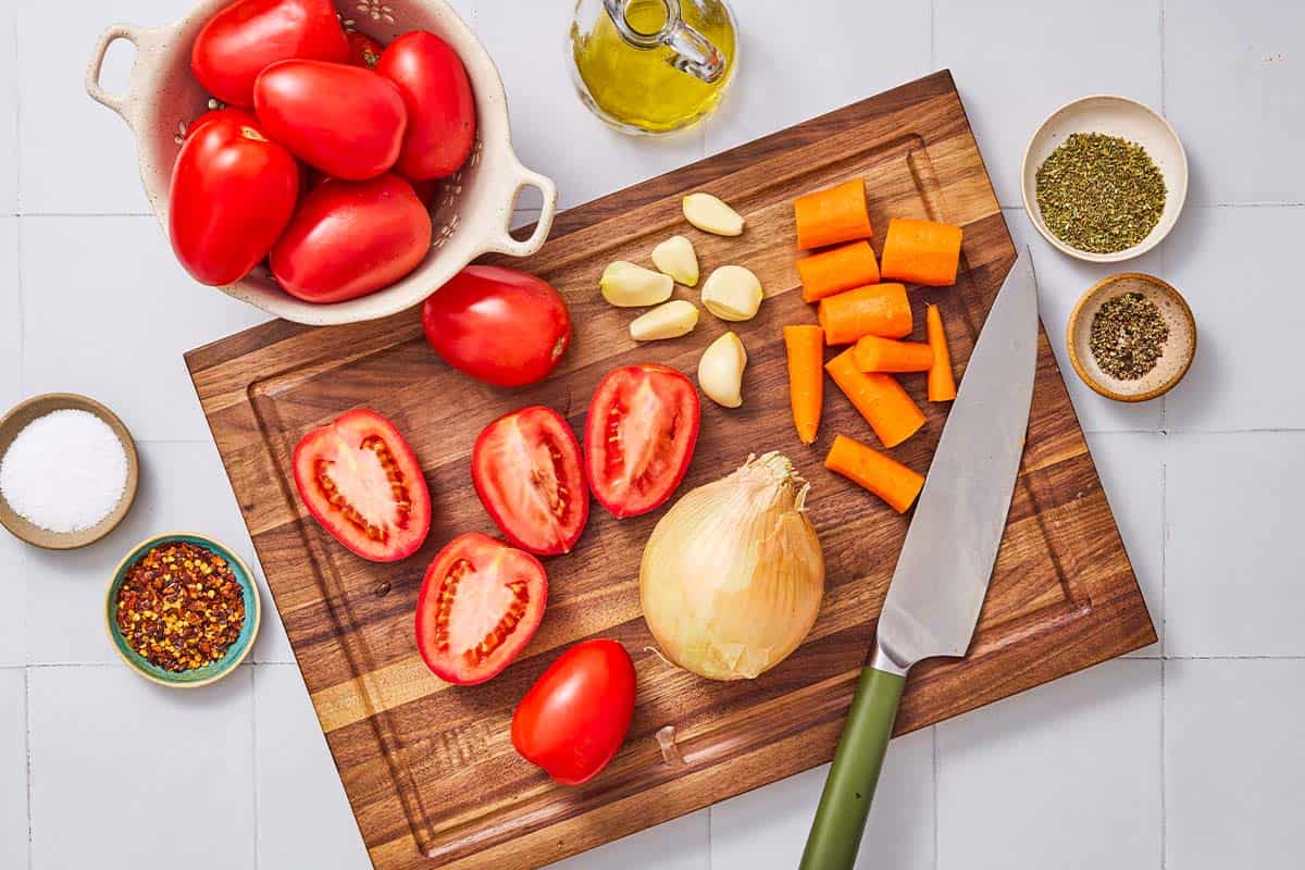 Ingredients for roasted tomato sauce including tomatoes, carrots, onion, garlic, olive oil salt, red pepper flakes, Italian seasoning and black pepper.